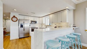 Une cuisine moderne avec des meubles blancs, un îlot central doté de tabourets et un réfrigérateur en acier inoxydable.