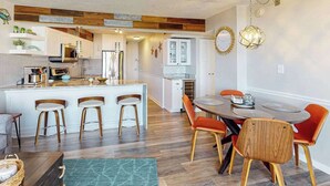 Eine moderne Küche mit Holzelementen, ein Essbereich mit orangefarbenen Stühlen und eine zentrale Kücheninsel mit Hockern.