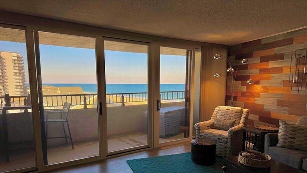 Ein Zimmer mit Blick auf den Strand, einer Schiebetür, einem gemusterten Teppich und einer Holzwand.