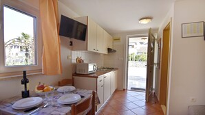 A compact kitchen with a dining table set for two, a microwave, and a television above the counter. - Cozy Ground-floor Apartment in Umag (Umag)