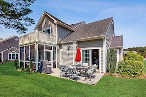 A two-story house with a covered patio, a grill, and a red umbrella.