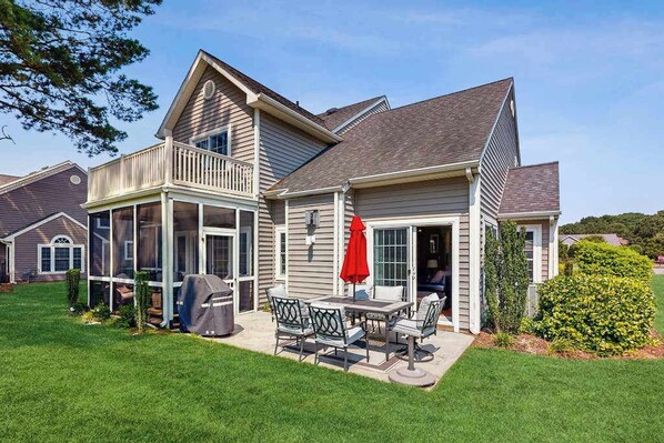 A two-story house with a covered patio, a grill, and a red umbrella.