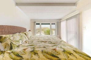 A bedroom with a bed, a window with blinds, and a view of greenery outside. - Inviting first-floor condo in Ocean City right on the beach (Ocean City)