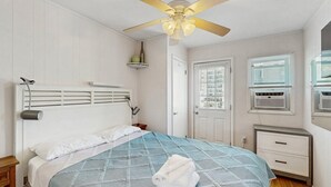 Ein Schlafzimmer mit Bett, Deckenventilator, Fenster mit Jalousien, Klimaanlage und Tür.