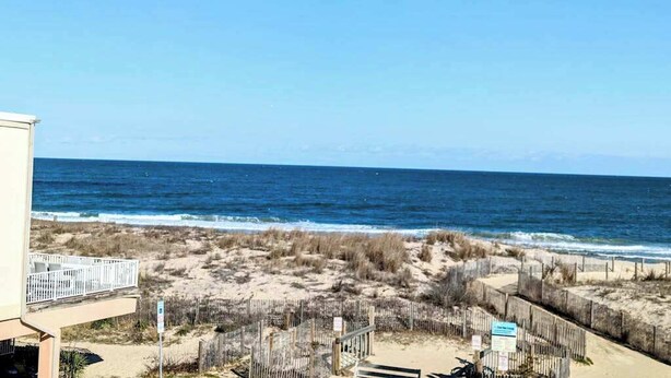 Blick auf einen Strand mit Zaun, einem Gebäude und wolkenlosem Himmel.