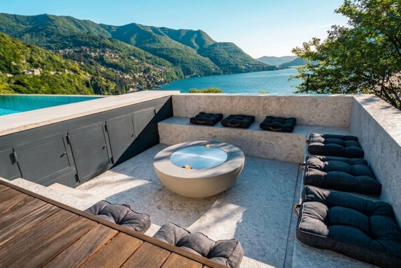 Een terras met een ingebouwd bubbelbad, zithoek en uitzicht op een meer en bergen.