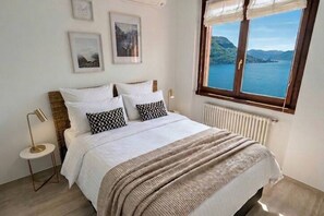 A bedroom with a bed, bedside tables, and a window with a view of the sea. - Palazzo Pognana with Infinity Pool and Lake Views (Pognana Lario)