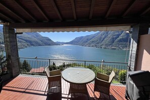 Ein überdachter Außenbereich mit Tisch und Stühlen, mit Blick auf einen See und Berge im Hintergrund.