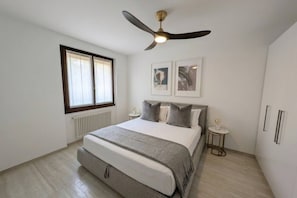 A bedroom with a bed, a ceiling fan, a window, and a small table with a lamp. - Palazzo Pognana with Infinity Pool and Lake Views (Pognana Lario)