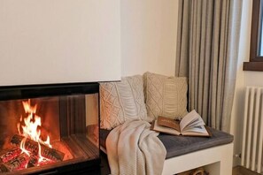 Ein gemütlicher Sitzbereich mit Kamin, einem Buch und einer Decke.