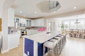 A modern kitchen with white cabinets, a central island with bar stools, and a dining area with a table and chairs. - Sunset Island - 57 Island Edge (Ocean City)