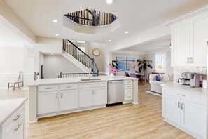 A spacious kitchen with a central island, a staircase leading to an upper level, and a dining area with a view. - Sunset Island - 57 Island Edge (Ocean City)
