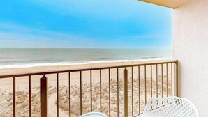 A balcony with a view of the beach, a white chair, and a small table. - Breezy beachfront condo with balcony, W/D, hot tub, & full kitchen (Ocean City)