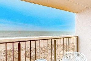 Ein Balkon mit Blick auf den Strand, ein weißer Stuhl und ein kleiner Tisch.