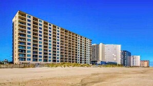 A multi-story hotel with a uniform facade, located near a beach with a clear sky. - Breezy beachfront condo with balcony, W/D, hot tub, & full kitchen (Ocean City)