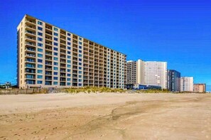 Ein mehrstöckiges Hotel mit einheitlicher Fassade in Strandnähe bei blauem Himmel.