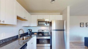 Una cocina compacta con armarios blancos, un refrigerador de acero inoxidable, un microondas, una estufa y un lavavajillas.