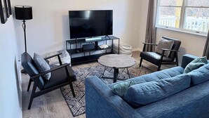 Una sala de estar moderna con una televisión de pantalla plana, un sofá, una mesa de centro y una lámpara de pie.