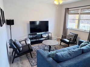 Ein modernes Wohnzimmer mit Flachbildfernseher, einer Couch, einem Couchtisch und einer Stehlampe.