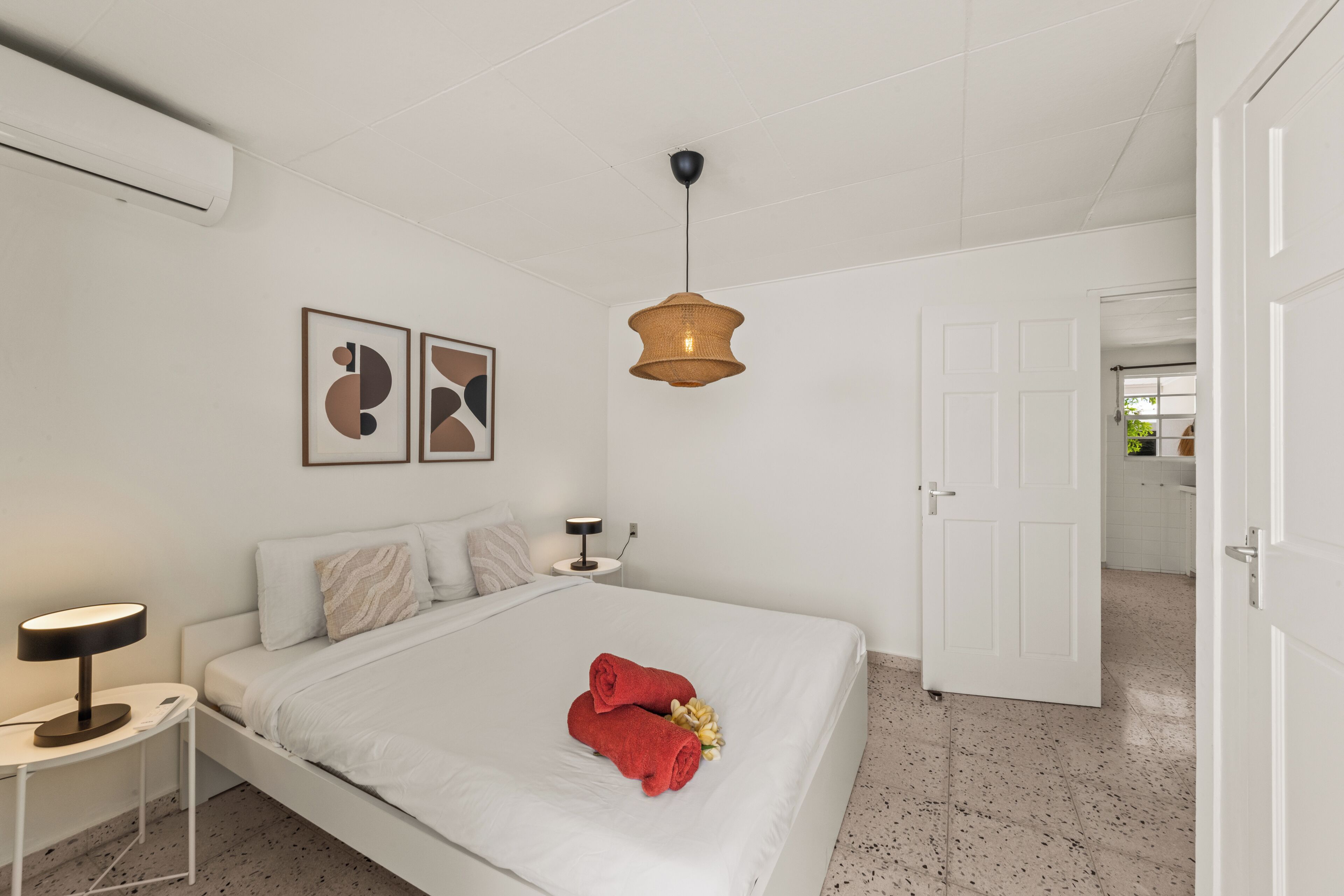 Una camera da letto con un letto, un comodino con una lampada, un lampadario e una porta che dà su un'altra stanza.