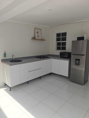 Una cocina moderna con armarios blancos, un refrigerador de acero inoxidable, una estufa a gas y un ventanal.