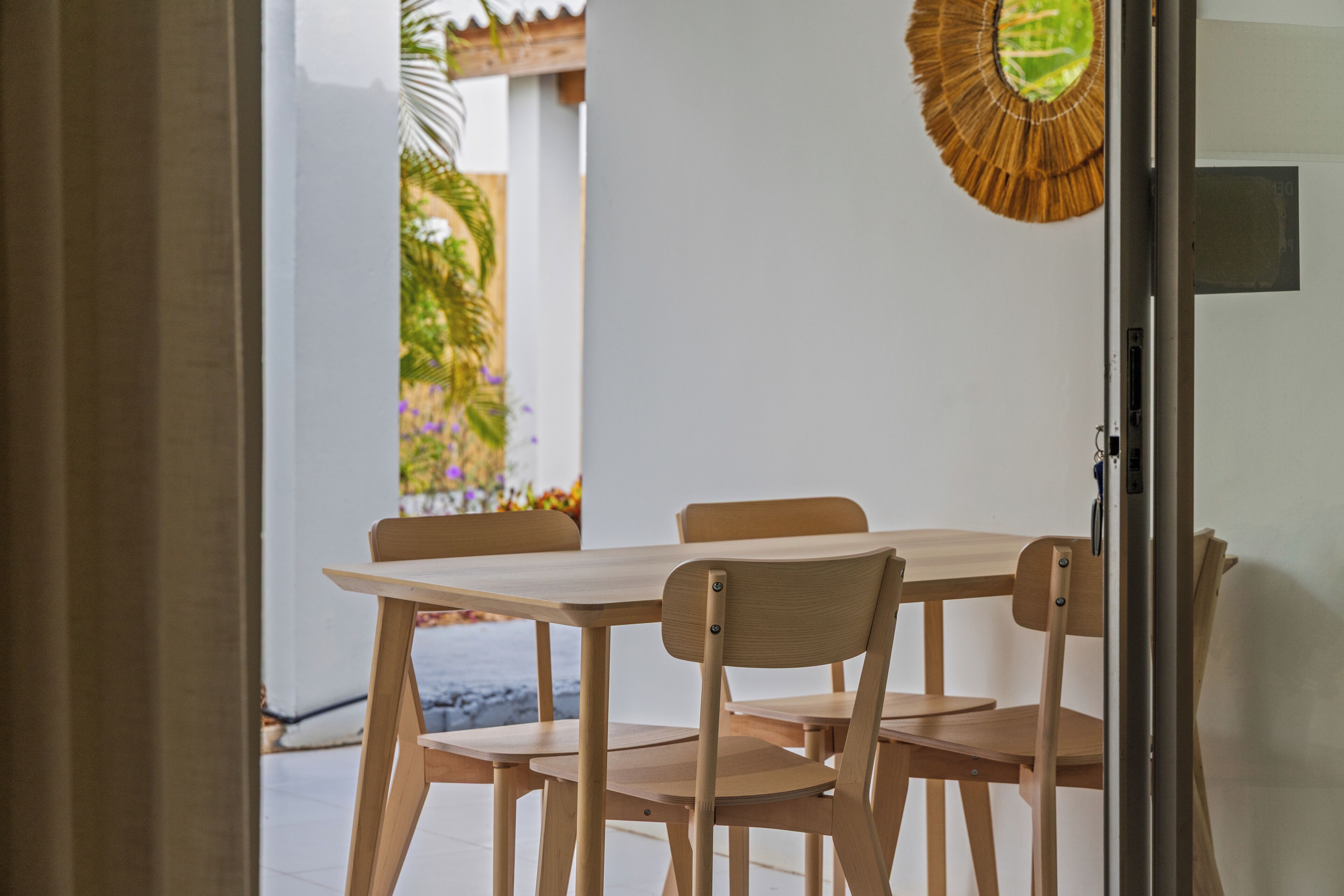 Ein Essbereich mit Holztisch und -stühlen, einem dekorativen Spiegel und Blick auf einen Garten durch eine geöffnete Tür.