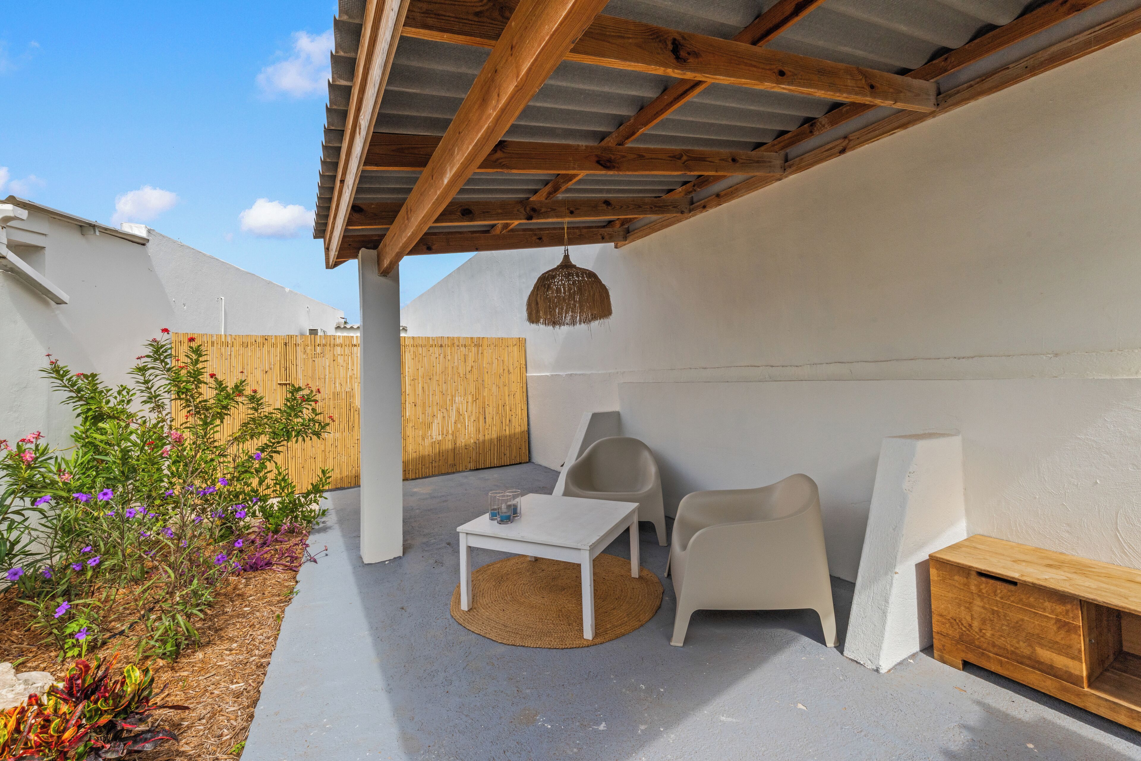 A covered outdoor patio with a table and chairs, a hanging light fixture, and a wooden bench.