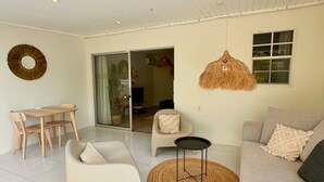 Uma sala de estar moderna com sofá, cadeiras, uma mesinha, luminária pendente e uma porta de vidro deslizante que dá para outro ambiente.