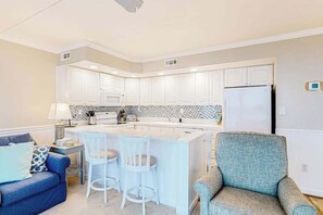A modern kitchen with white cabinets, a central island with bar stools, and a refrigerator. - Oceanfront, 2nd-floor condo with gorgeous view, balcony, pool & great location (Ocean City)