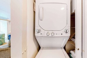 A white washing machine in a laundry room with a door, a towel rack, and a green chair visible. - Oceanfront, 2nd-floor condo with gorgeous view, balcony, pool & great location (Ocean City)
