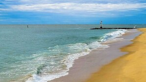 A beach with clear water, a sandy shore, and a lighthouse in the distance. - Bahama Princess I (Ocean City)