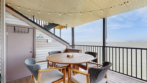 A covered outdoor seating area with a table and chairs, a staircase, and a view of the sea. - Bahama Princess I (Ocean City)