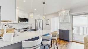 A modern kitchen with white cabinetry, a central island with bar stools, stainless steel appliances, and pendant lighting. - Bahama Princess I (Ocean City)