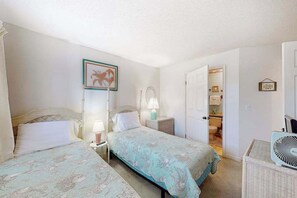 Quarto com duas camas, uma mesa de cabeceira com abajur, um quadro na parede e uma porta para o banheiro.