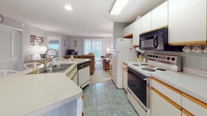 A compact kitchen with a microwave, stove, and sink. There is a dining area with a table and chairs. - Coastal condo with a private washer/dryer, central AC, and a shared pool (Ocean City)