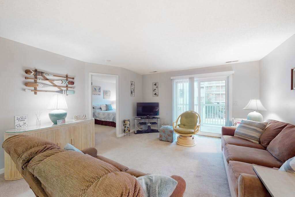 A living room with a sofa, armchair, TV, and a glass door leading to a balcony.