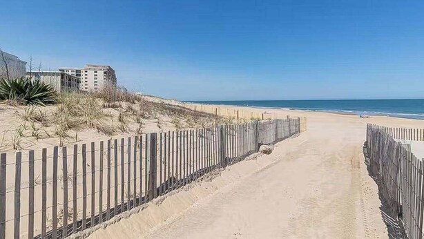 A sandy beach path with a wooden fence, leading to a beach with a clear blue sky. - Coastal condo with a private washer/dryer, central AC, and a shared pool (Ocean City)