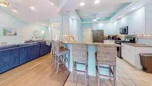 A modern kitchen with white cabinets, a central island, and bar stools. - Turtle Shores-22 Boston (Ocean Pines)