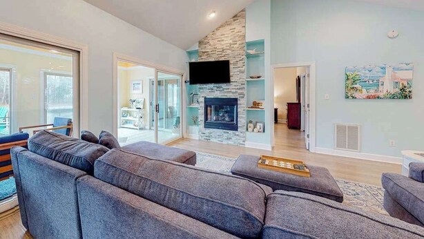 A spacious living room with a stone fireplace, grey sofas, and a flat-screen TV mounted on the wall. - Turtle Shores-22 Boston (Ocean Pines)