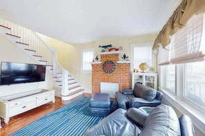 Ein Wohnzimmer mit Fernseher, Ledersofa, Kamin aus Backsteinen und einer Treppe.