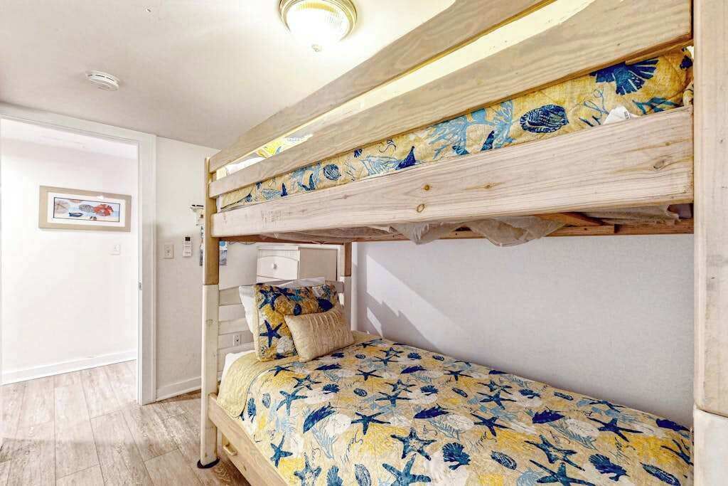 Un lit superposé avec une couvre-lit à motifs floraux, une table de chevet avec une lampe et un tableau encadré au mur.