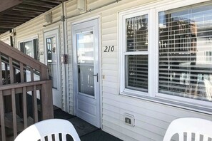 Una fila de cabañas blancas con puertas numeradas, una terraza de madera y una ventana con persianas.
