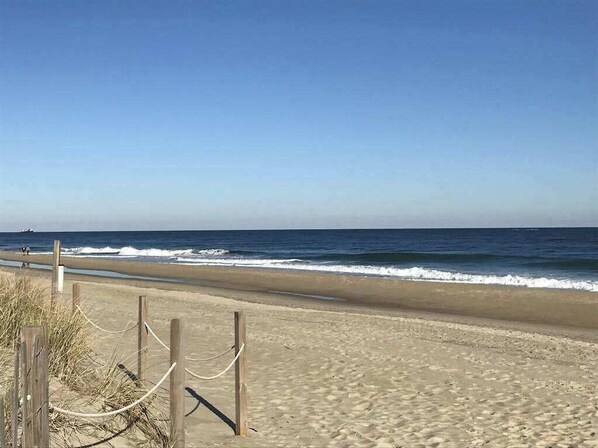 Una playa con valla de madera, cielo despejado y olas del océano.