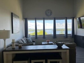 Una habitación con vista a un lago, un reloj en la pared, un sofá y una mesa con una lámpara.