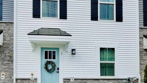 Une maison à deux étages avec une porte d’entrée bleu clair, une guirlande et une petite fenêtre avec un rideau.
