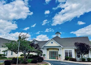 Un bâtiment avec une porte verte, un petit porche et un ciel bleu clair parsemé de nuages.
