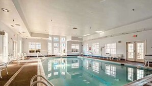 Une piscine intérieure à l’eau claire, entourée de murs et de fenêtres blancs.