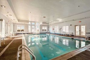 Une piscine intérieure à l’eau claire, entourée de murs et de fenêtres blancs.