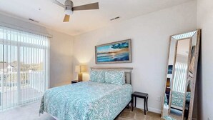 A bedroom with a bed, a nightstand, a lamp, a ceiling fan, a painting, and a large mirror. - Seaside Village Bowline 13007 -2 (West Ocean City)