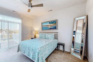A bedroom with a bed, a nightstand, a lamp, a ceiling fan, a painting, and a large mirror. - Seaside Village Bowline  13007 -2 (West Ocean City)